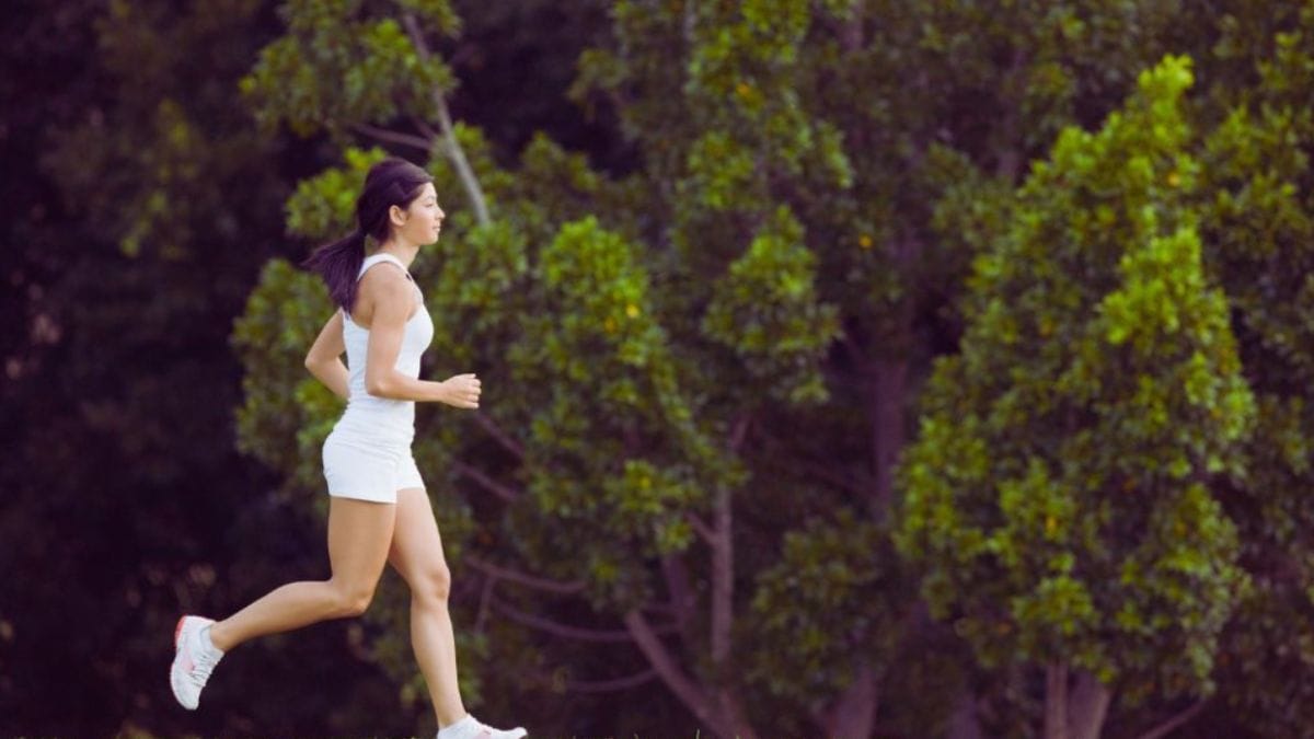 Subconscious Reframing Temecula, CA: Which Daily Habits Improve Mental Clarity? 2 Woman jogging outdoors in a lush green park, wearing white athletic clothing, representing daily exercise to support mental clarity and subconscious reframing.