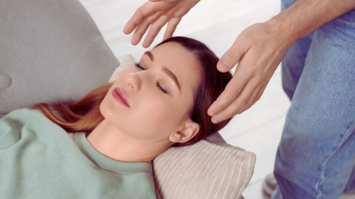 Subconscious Reframing Temecula, CA: Which Daily Habits Improve Mental Clarity? 3 Woman lying back on a pillow while a practitioner gently holds their hands near her head, illustrating a calming subconscious reframing session in a Temecula, CA wellness setting.