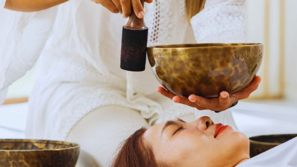 Vibrational Healing in Temecula, CA: Grounded Sound and Energy Work With Tina Foran 2 Close-up of a practitioner in white clothing holding a large metal singing bowl and mallet above a client’s head during a vibrational healing session in Temecula, California.