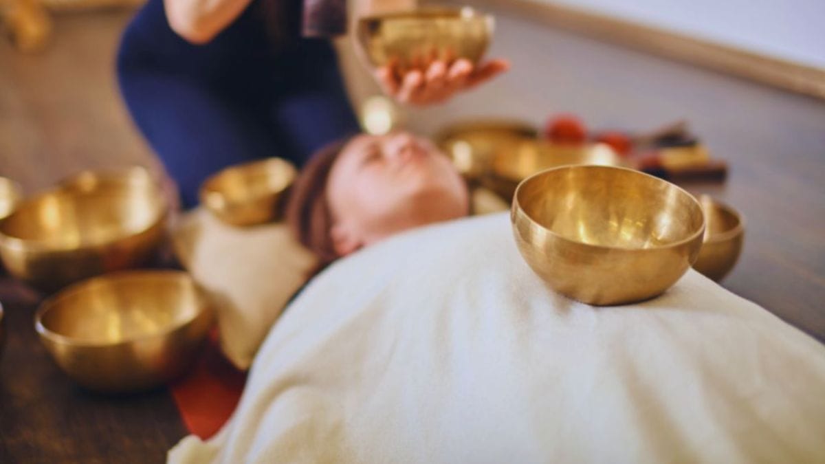 Vibrational Healing in Temecula, CA: Grounded Sound and Energy Work With Tina Foran 1 Practitioner performing vibrational sound healing with a metal singing bowl over a relaxed client lying on a cushion, illustrating a vibrational sound session in the Temecula area.